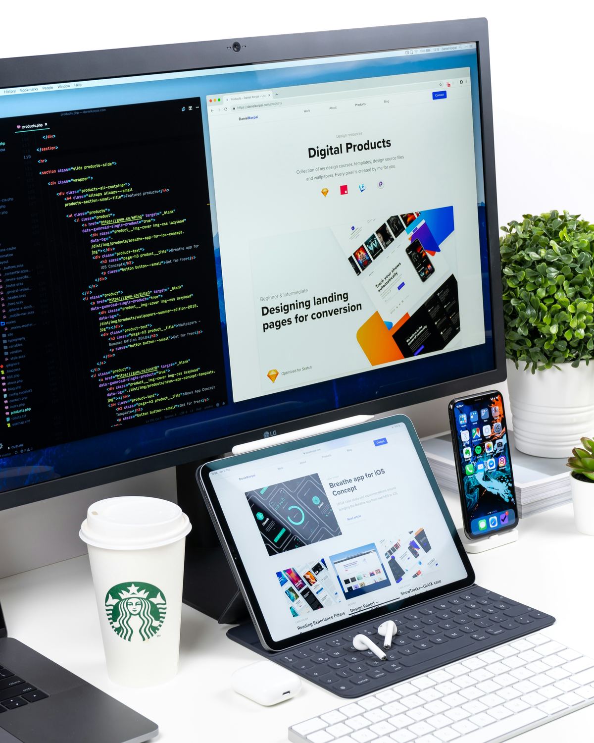 Desk setup with an iMac and MacBook showing design and code work, a Starbucks cup, and a plant